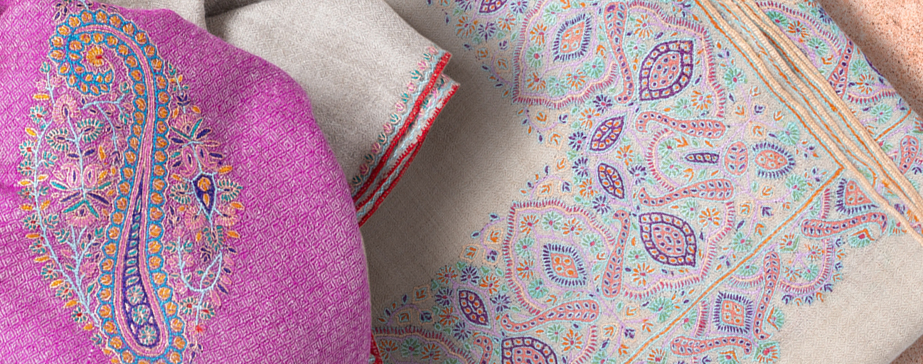 Pashmina shawls in shades of cream and pink with complex embroidered borders.