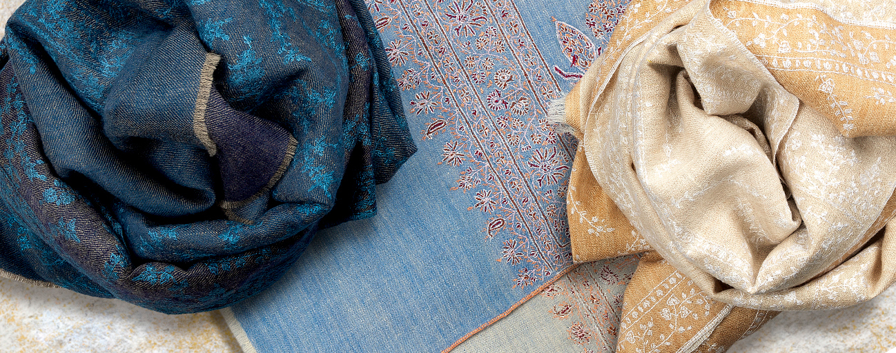 Three embroidered reversible pashmina shawls in blues and whites.