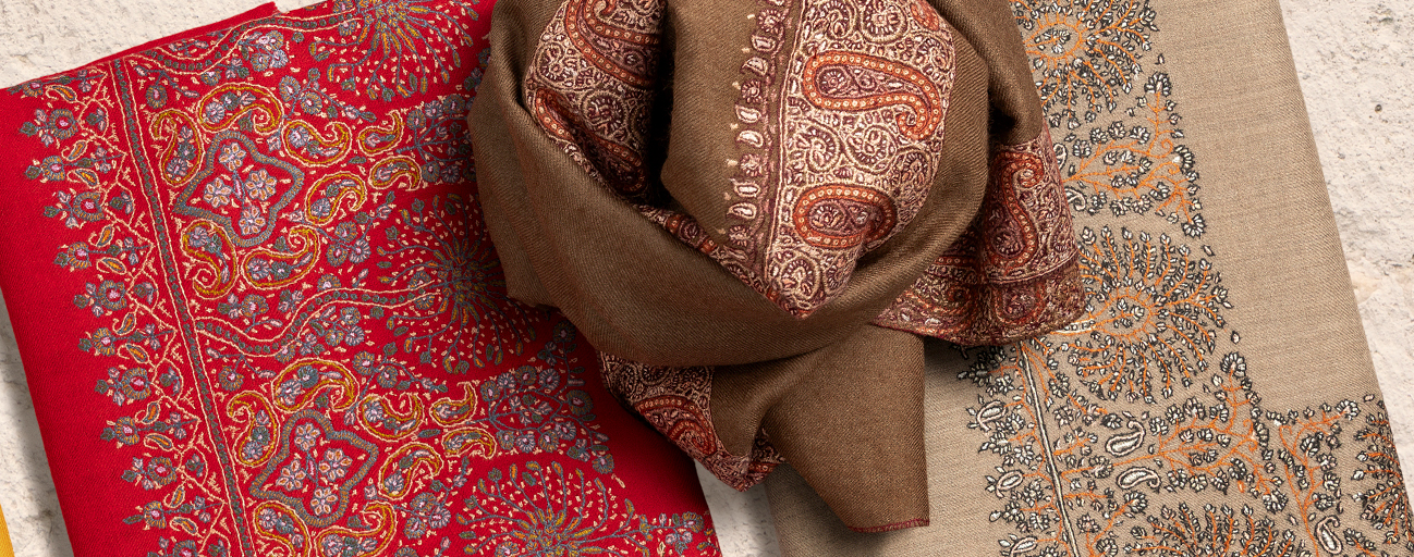 Three pashmina shawls in shades of red and brown with embroidered borders.
