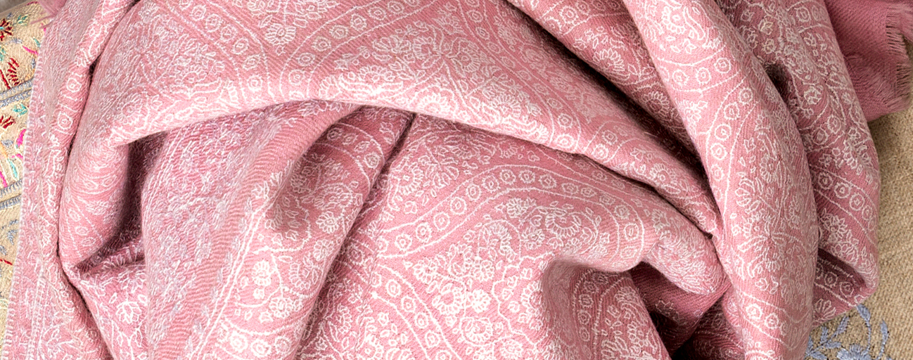 An intricately embroidered jamawar pashmina shawl in pale pink and white.